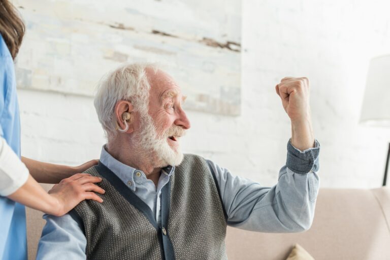 Happy senior man with hearing aid looking away, sitting at home